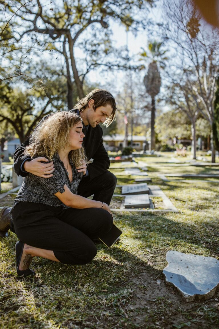A couple mourning at a cemetery during the day, expressing loss and sadness.