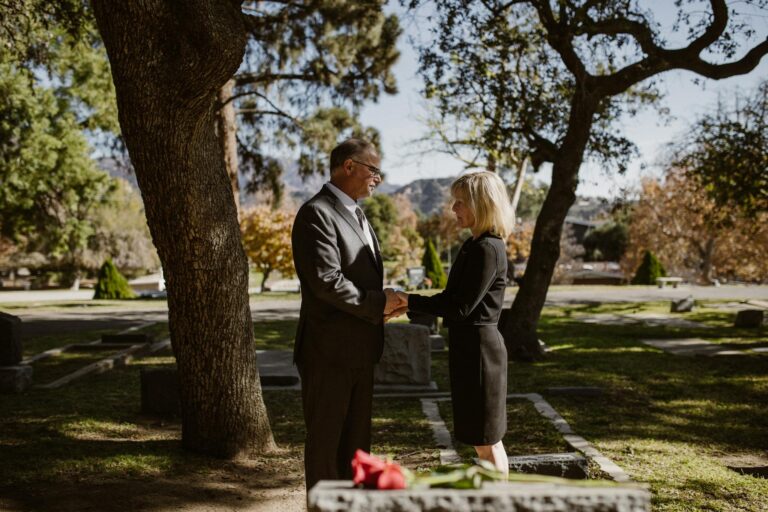 An elderly couple shares a moment of togetherness in a serene cemetery setting.