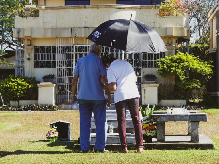 Elderly couple standing together with an umbrella at a graveyard in Manila, Philippines.